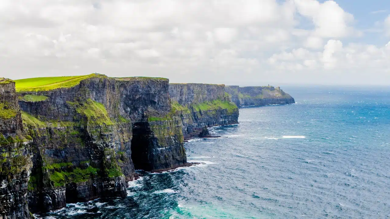 Rugged cliffs along the Atlantic coastline near Shannon, Ireland with grassy fields and waves crashing below